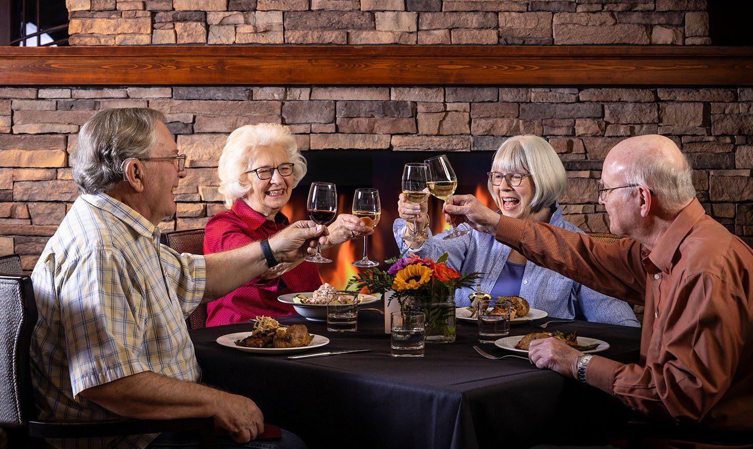 Four seniors toasting with wine glasses at dinner in The Terraces of Boise dining room