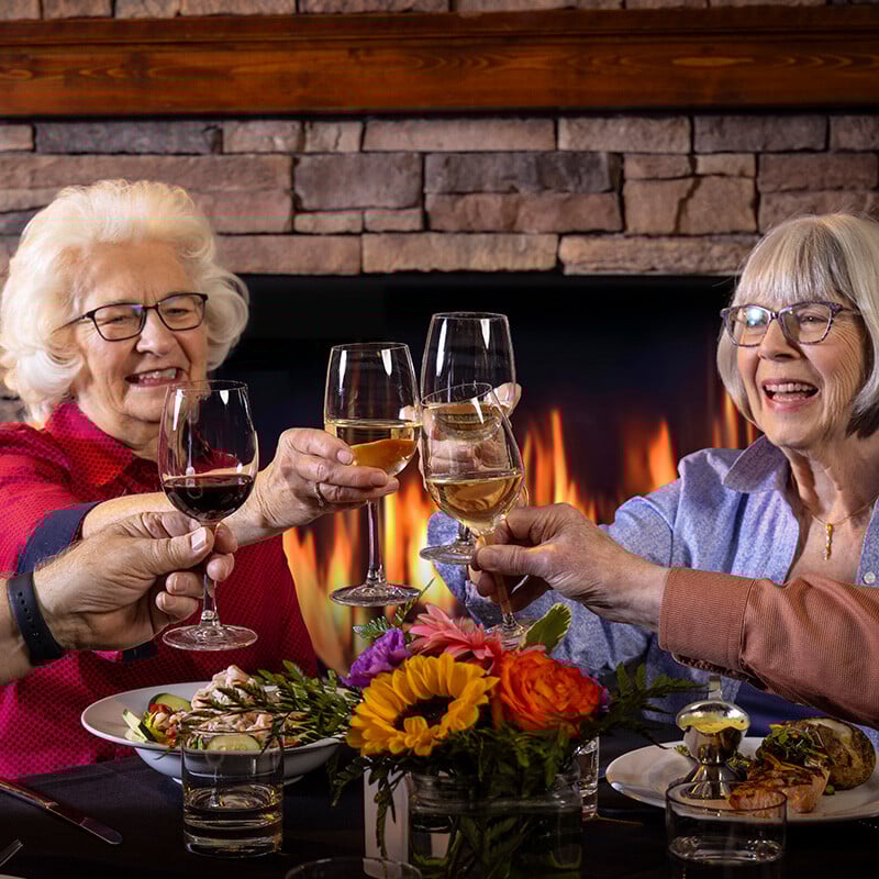Four seniors toasting with wine glasses at dinner in The Terraces of Boise dining room