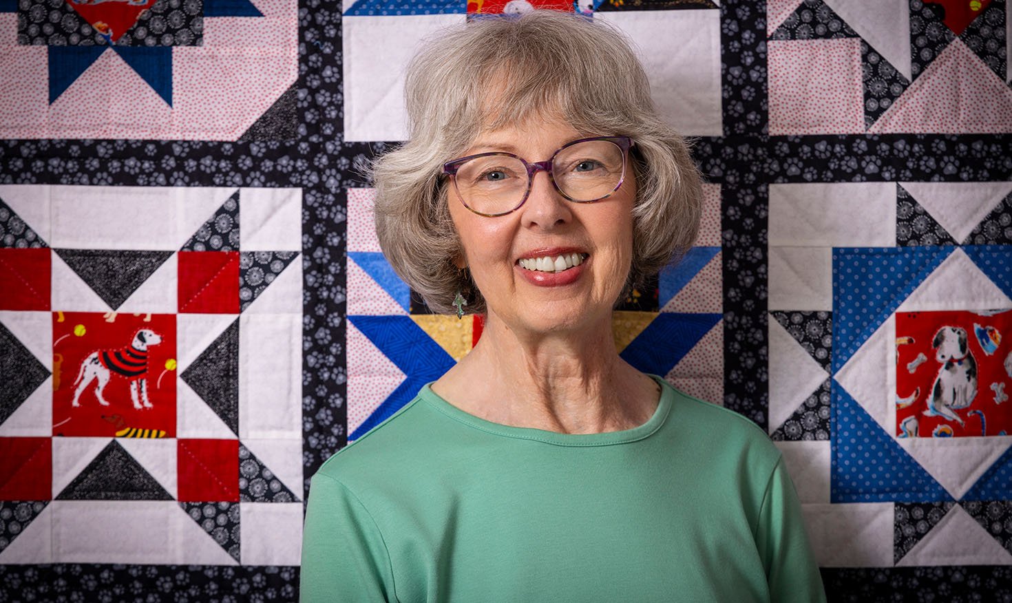 Smiling senior woman standing in front of a quilt