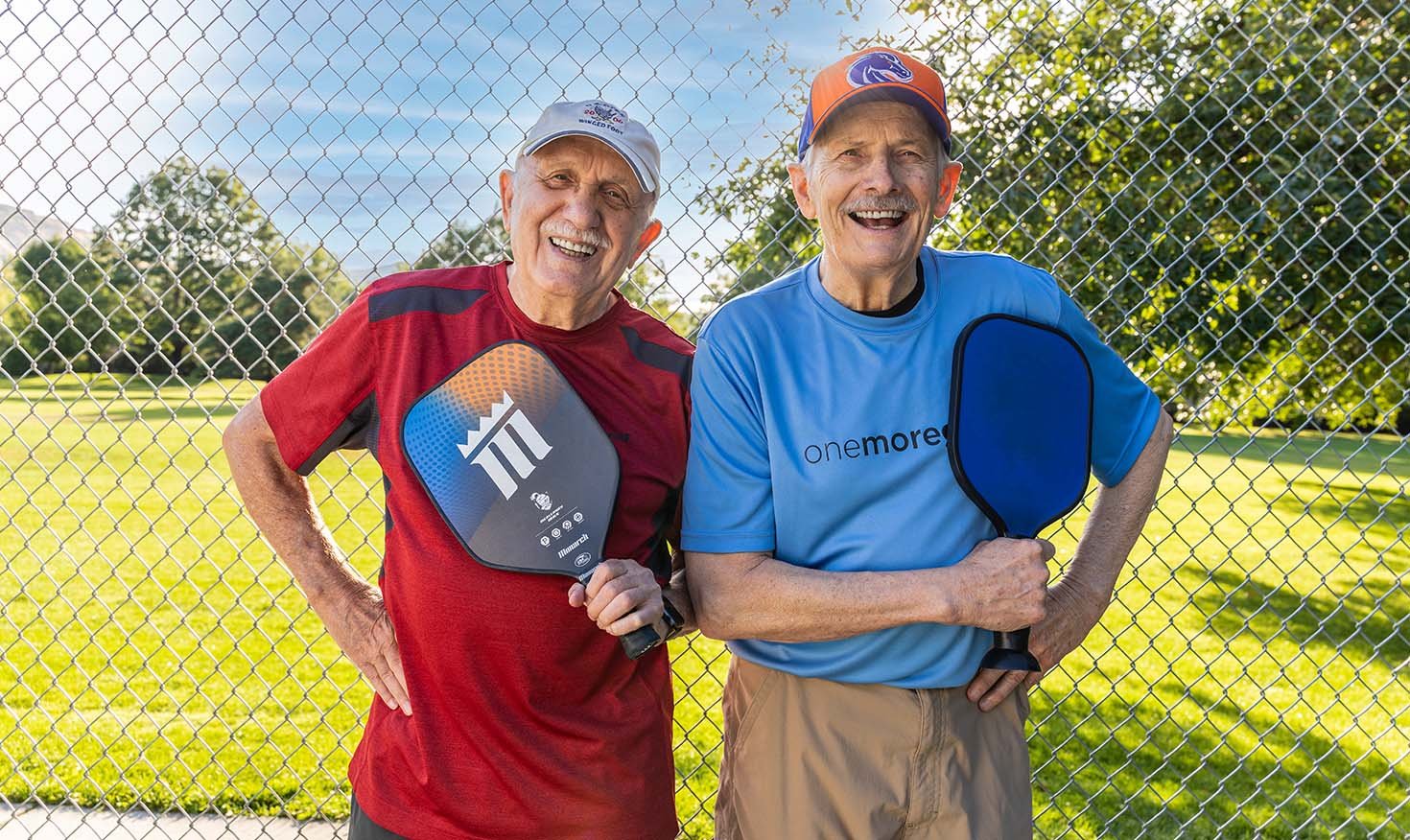 Two senior men holding up pickleball paddles
