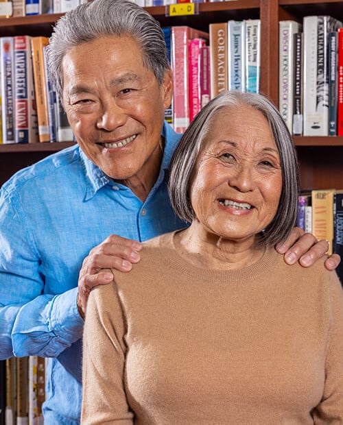 Senior man with his hands on the shoulders of a senior woman in front of a bookshelf in the library