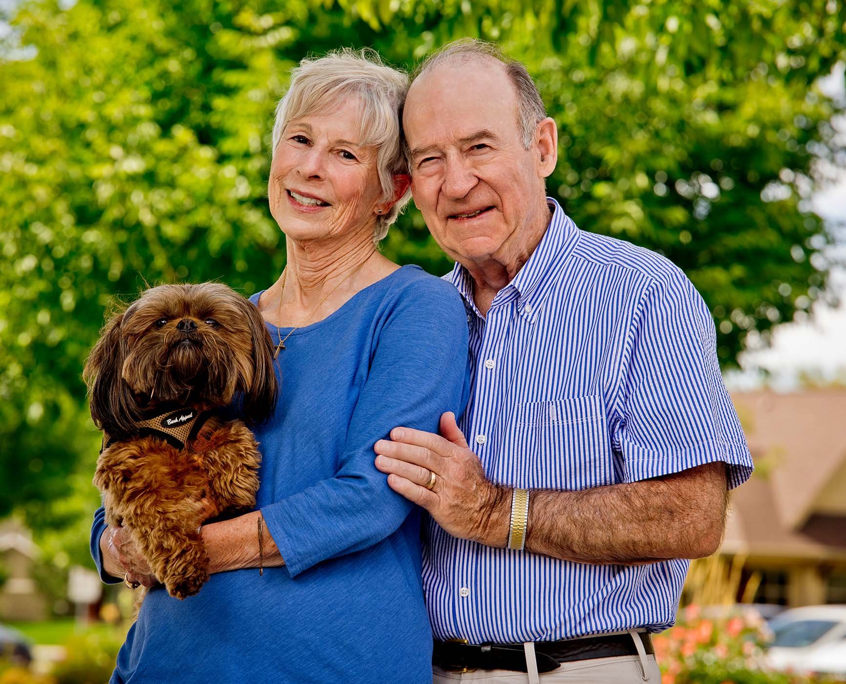 Senior couple standing outside and holding small brown dog