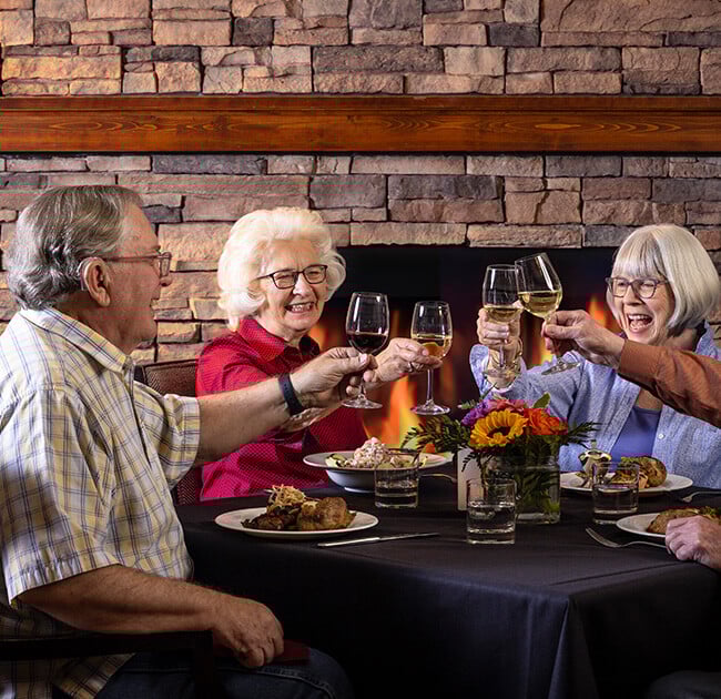 Four seniors toasting with wine glasses at dinner in The Terraces of Boise dining room