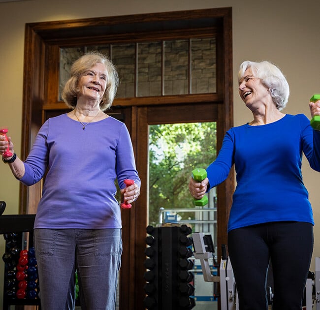 Two senior women lifting light weights in the fitness center