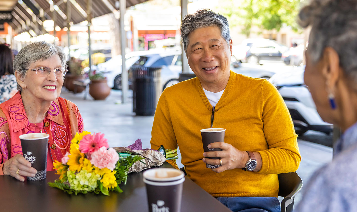 Two senior women and a senior man having coffee together on the patio of a shopping center