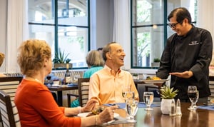 Dining room staff serving food to a senior man in the main dining room of The Terraces of Los Gatos