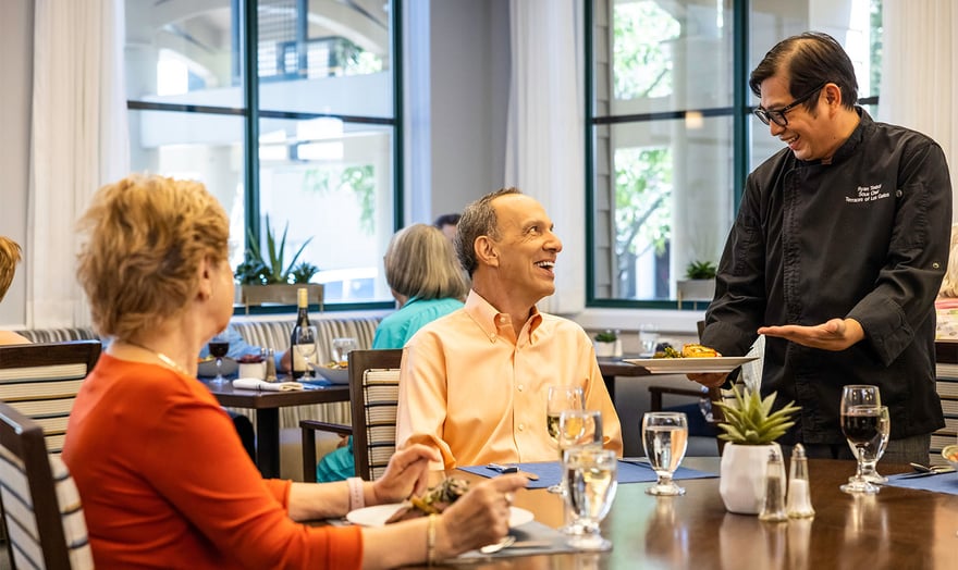 Dining room staff serving food to a senior man in the main dining room of The Terraces of Los Gatos