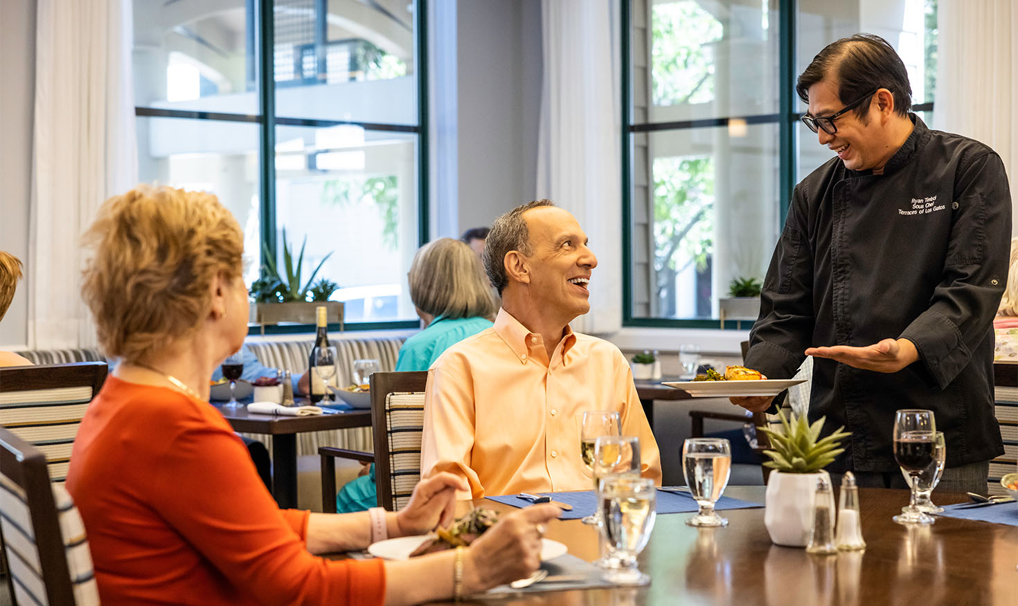 Dining room staff serving food to a senior man in the main dining room of The Terraces of Los Gatos