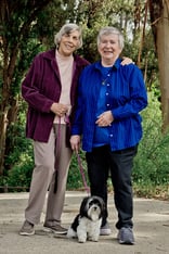 Two senior women posing with a black-and-white Havanese dog