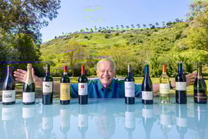 Senior man standing behind a collection of 10 wine bottles