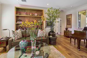 Living room with grand piano, couch, round glass coffee table, plants and large wooden bookshelf