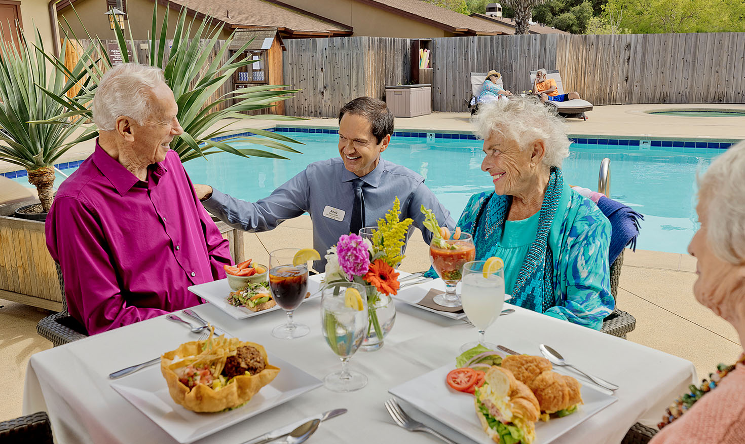 Valle Verde team member talking to a group of senior friends dining by the pool