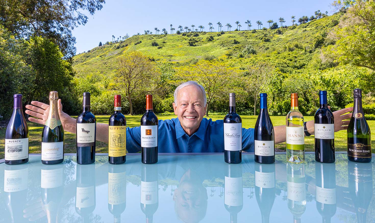 Senior man standing behind a collection of 10 wine bottles