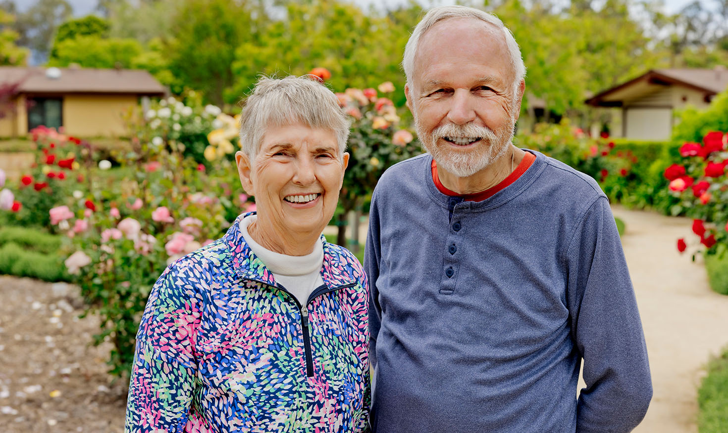 Smiling senior couple standing in front of rose bushes