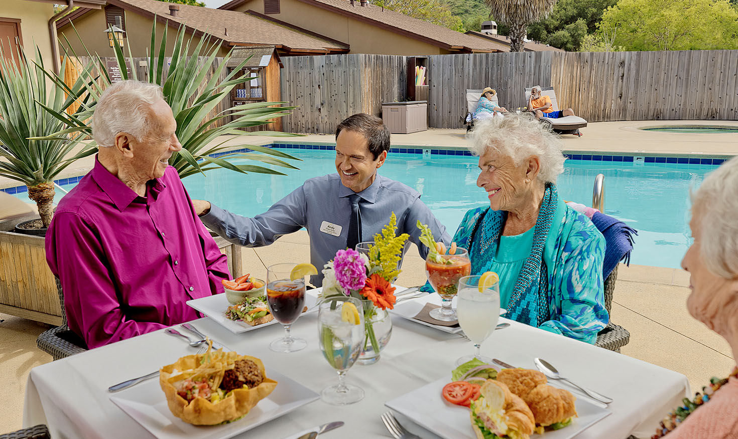 Valle Verde team member talking to a group of senior friends dining by the pool
