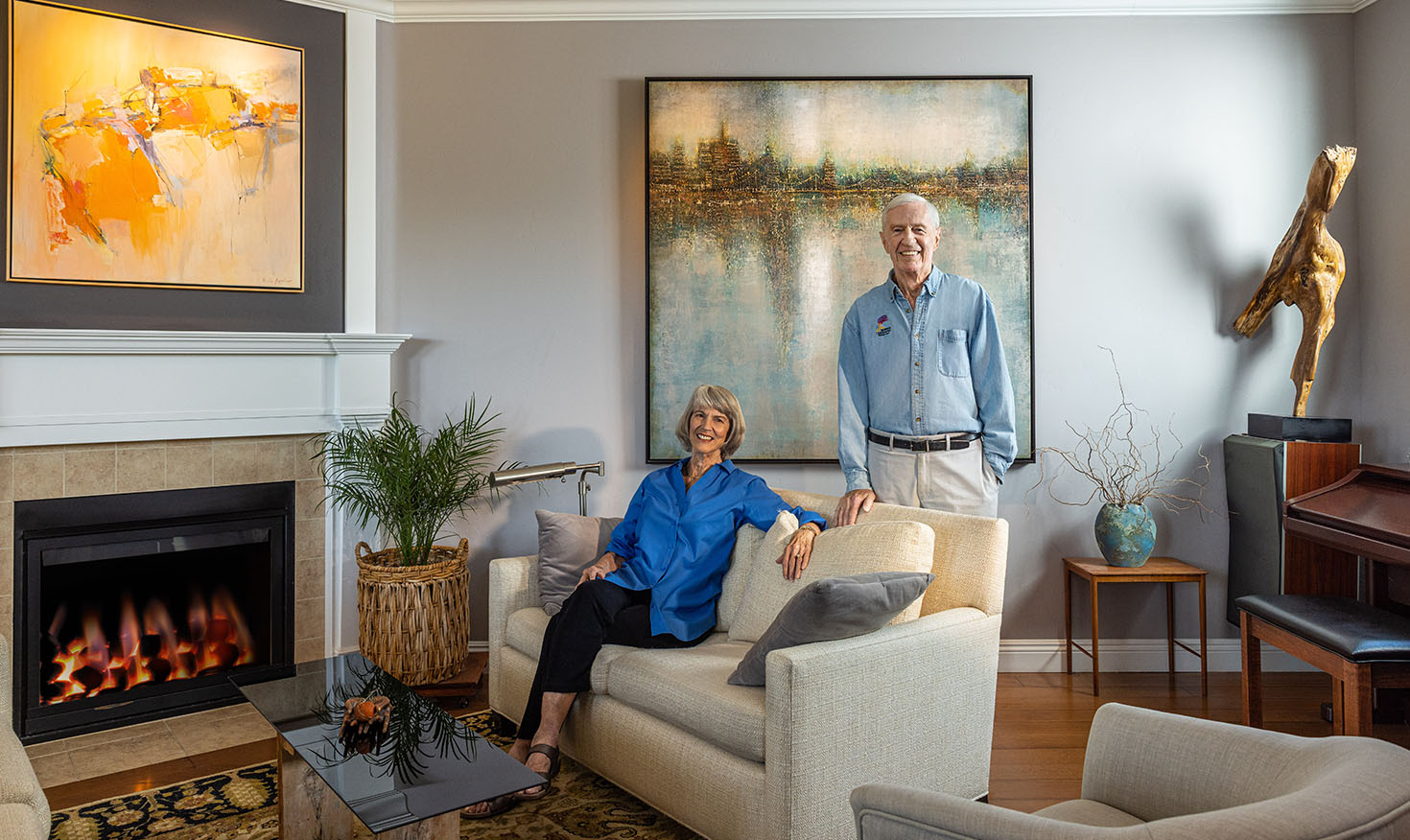 Senior woman sitting and senior man standing in the living room of their home in front of the fireplace