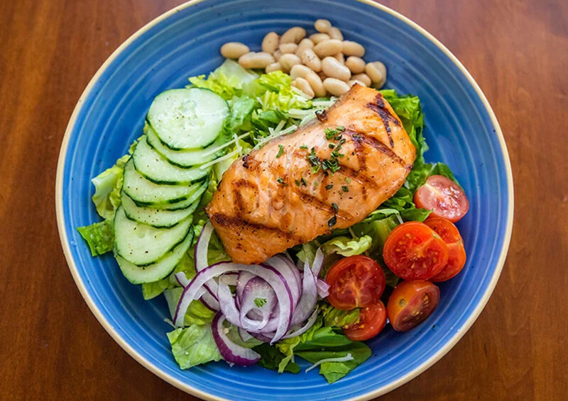 Salmon filet on a bed of lettuce, cucumber, onion, tomato and beans