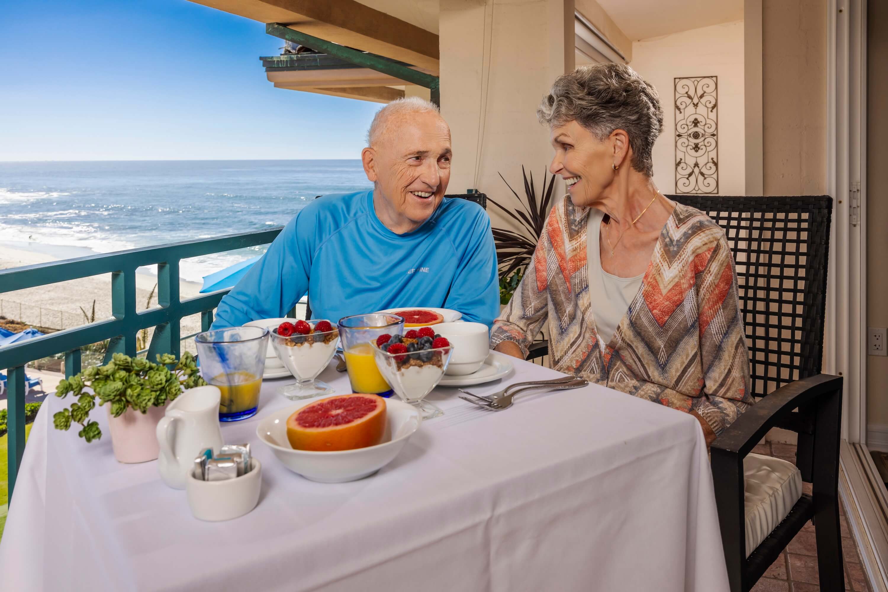 Senior couple enjoying breakfast on a balcony overlooking the ocean.