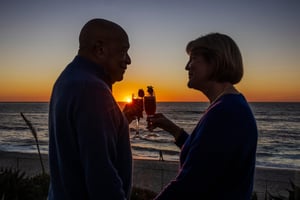 Two people silhouetted against an ocean sunset, holding drinks.
