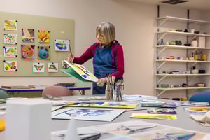 Resident in an art room painting with watercolors, surrounded by art supplies and displayed artwork.