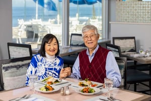 couple holding hands at a restaurant table with meals and ocean view.