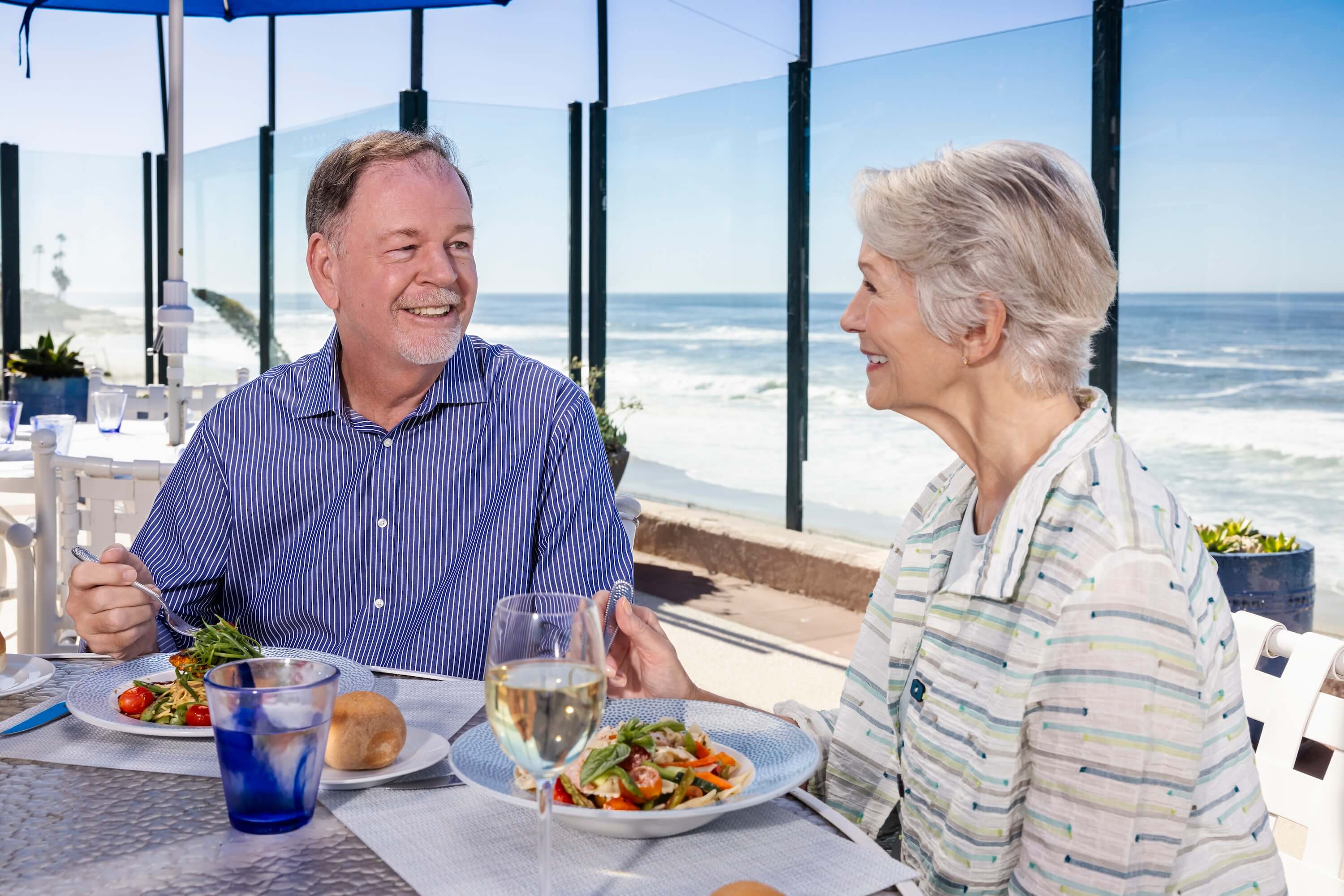 A senior couple dining outdoors with an ocean view.