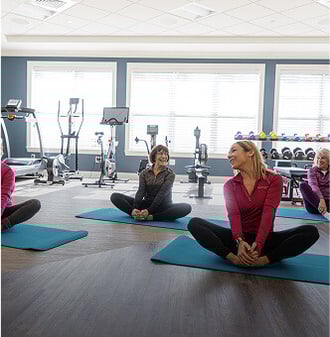 Group of senior women sitting on yoga mats in a HumanGood Life Plan Community fitness center