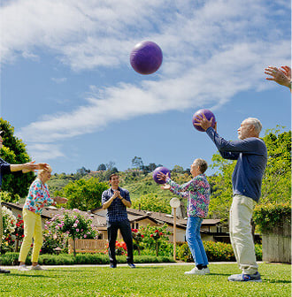 Group of seniors at a HumanGood Life Plan Community playing with purple balls on the lawn