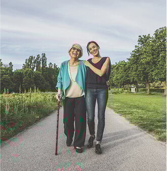 Senior woman with a cane walking with her adult daughter on a path in a HumanGood Life Plan Community