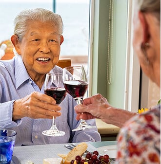 Seniors toasting with glasses of red wine in the dining room of a HumanGood Life Plan Community