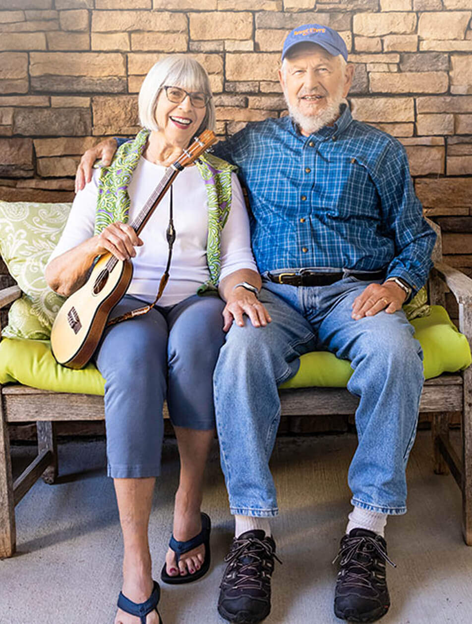 Senior couple sitting on an outdoor bench in front of a brick wall
