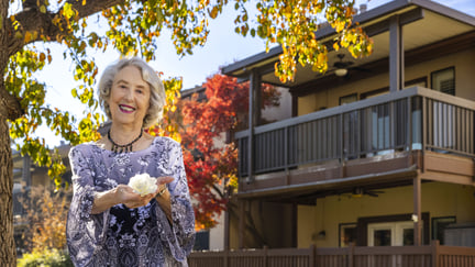 senior woman holding a flower in front of apartment building