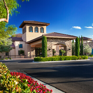 A modern, upscale building with stone accents, surrounded by lush greenery and vibrant red flowers, under a clear blue sky, conveying elegance and tranquility.