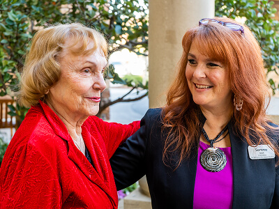 Two women smiling warmly at each other outdoors.