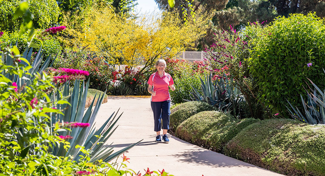 Female resident walking on a path through the garden at a HumanGood Life Plan Community