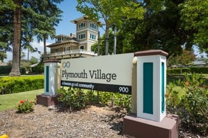 Plymouth Village sign at the entrance to the community with a large house in the background