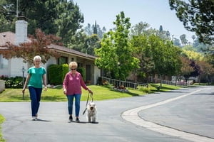 Two senior women walking with a dog around the Plymouth Village Life Plan Community