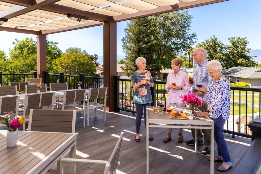 Two senior men and two senior women enjoying drinks and snacks on the Plymouth Village dining deck