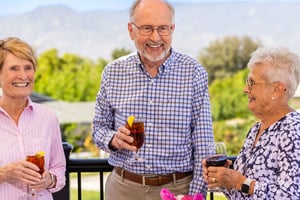 Two senior women and a senior man holding drinks and socializing on the Plymouth Village dining deck