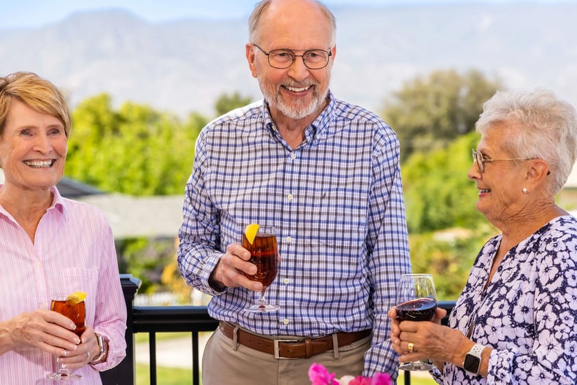 Two senior women and a senior man holding drinks and socializing on the Plymouth Village dining deck