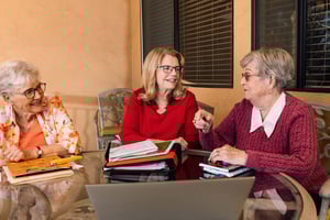 Three senior women with notebooks sit around a table during a writers' group meeting at Plymouth Village