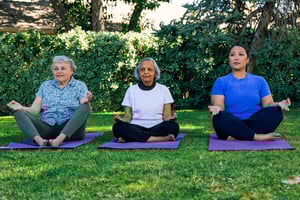 Three women sitting on yoga mats outdoors at Plymouth Village