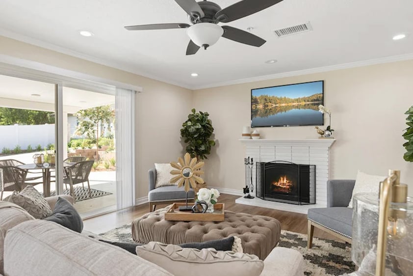 Living room with a TV hanging over a fireplace and sliding glass doors leading to a patio of a home at Plymouth Village