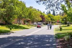Senior man and woman walking around Plymouth Village and another senior couple riding in a red golf cart