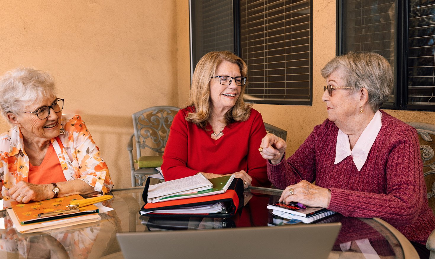 Three senior women with notebooks sit around a table during a writing group meeting at Plymouth Village