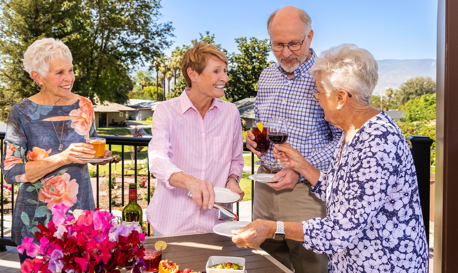 Three senior women and a senior man enjoying drinks and snacks on a deck at Plymouth Village