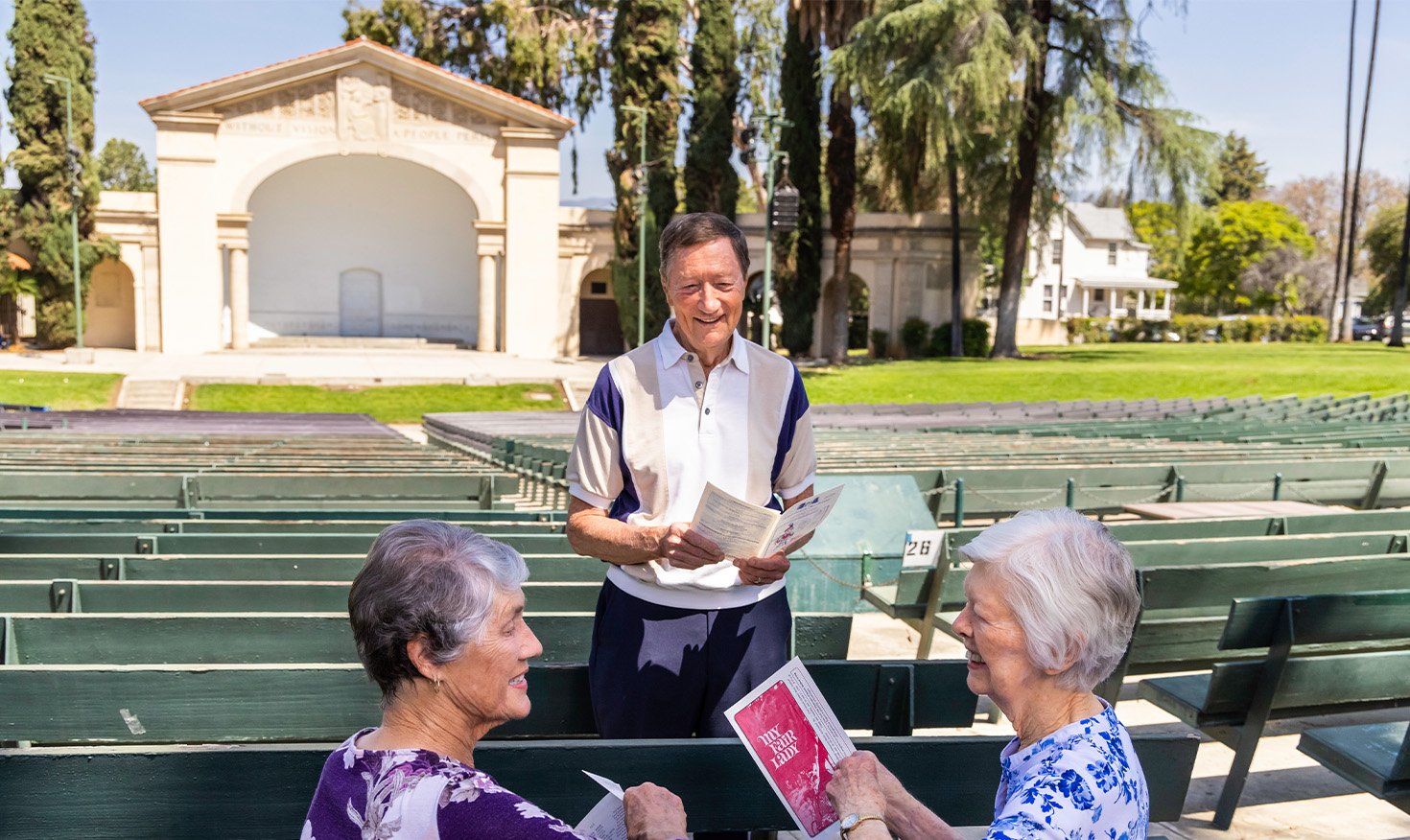 Two senior women and a senior man at an outdoor amphitheater holding programs from an event