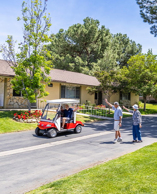 Senior man and woman walking around Plymouth Village waving at a senior couple in a red golf cart