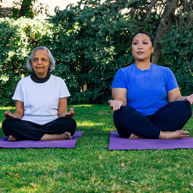 Two women sitting on yoga mats outdoors at Plymouth Village