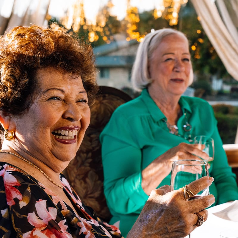 Two senior women with glasses of wine on the outdoor dining deck at Plymouth Village